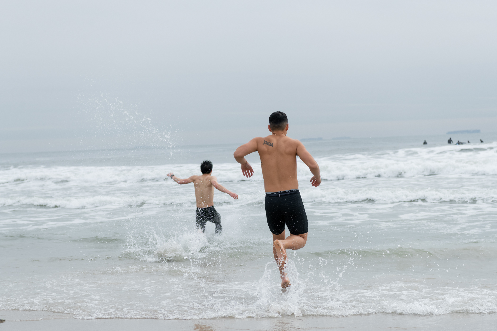 photo of two men running into the ocean